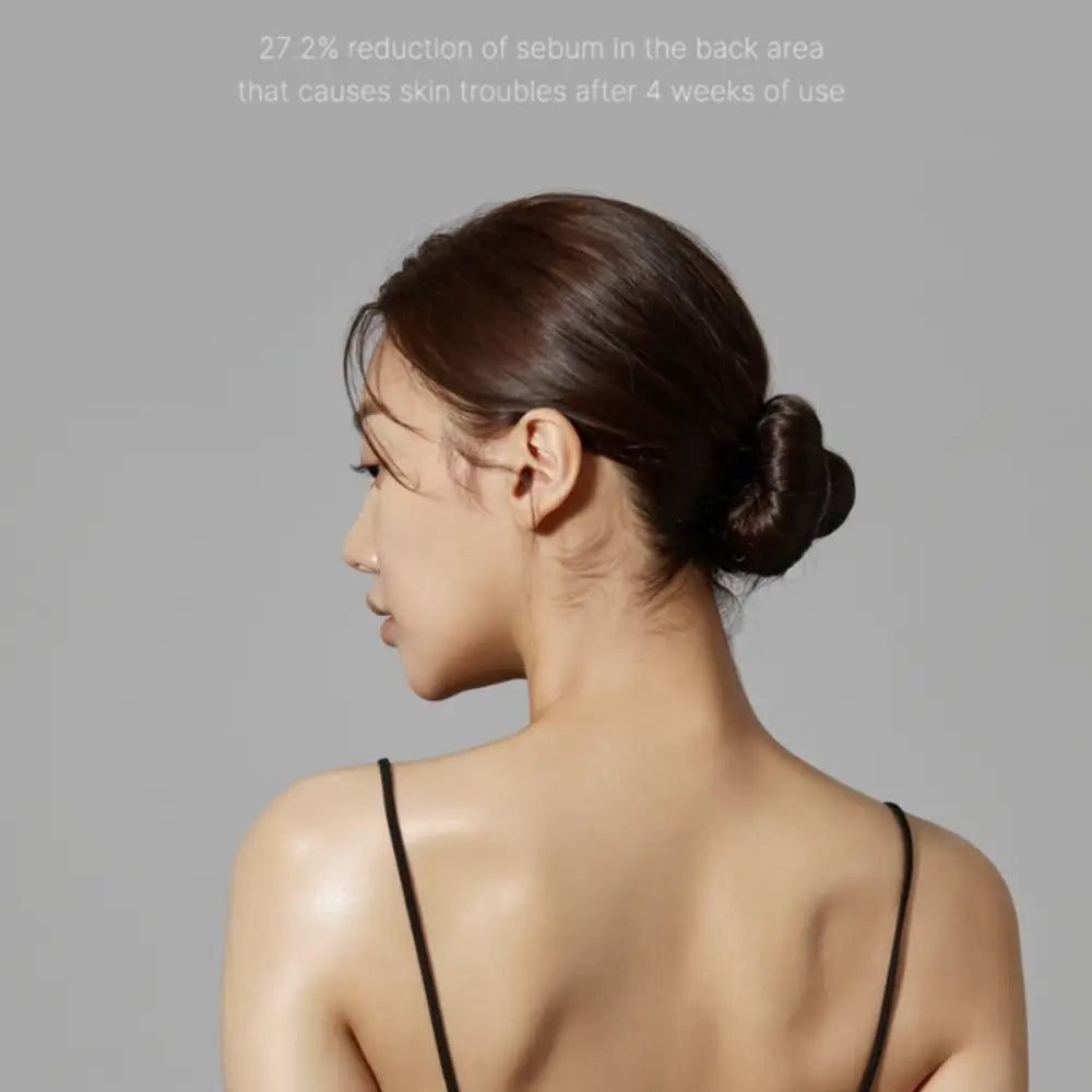 A woman with dark brown hair in a bun wearing a black top holding red clear cica body mist 200ml spray bottle
