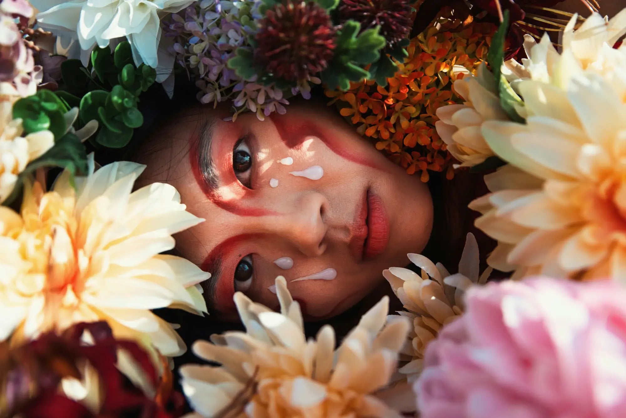A person with dramatic makeup and white paint tears surrounded by colorful flowers illustrating korean skincare south africa routine order