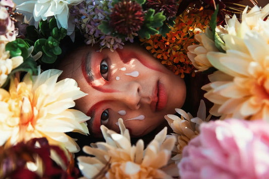 A person with dramatic makeup and white paint tears surrounded by colorful flowers illustrating korean skincare south africa routine order