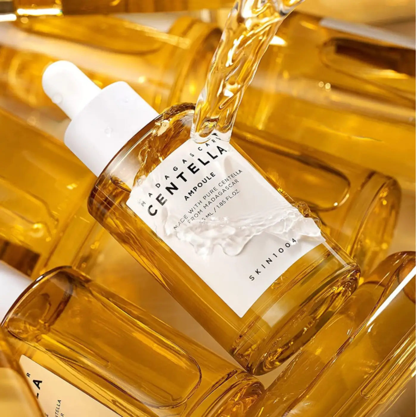 A clear glass bottle of madagascar centella ampoule 55ml with white dropper cap containing golden-yellow centella asiatica extract