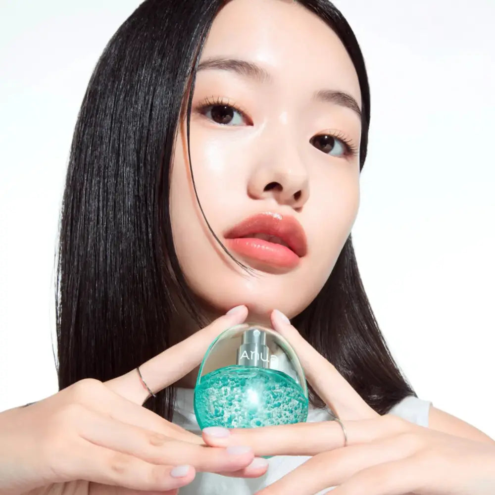 A translucent teal glass pdrn collagen glow serum spray bottle with a silver cap held delicately by hands