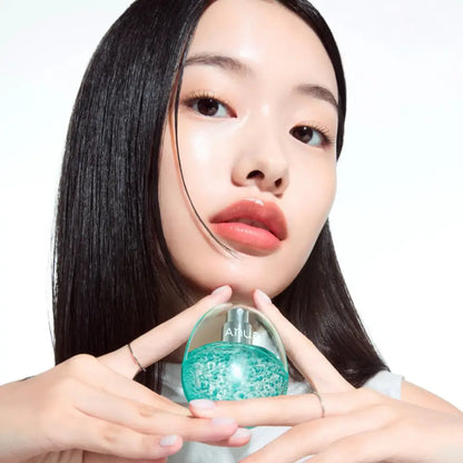 A translucent teal glass pdrn collagen glow serum spray bottle with a silver cap held delicately by hands