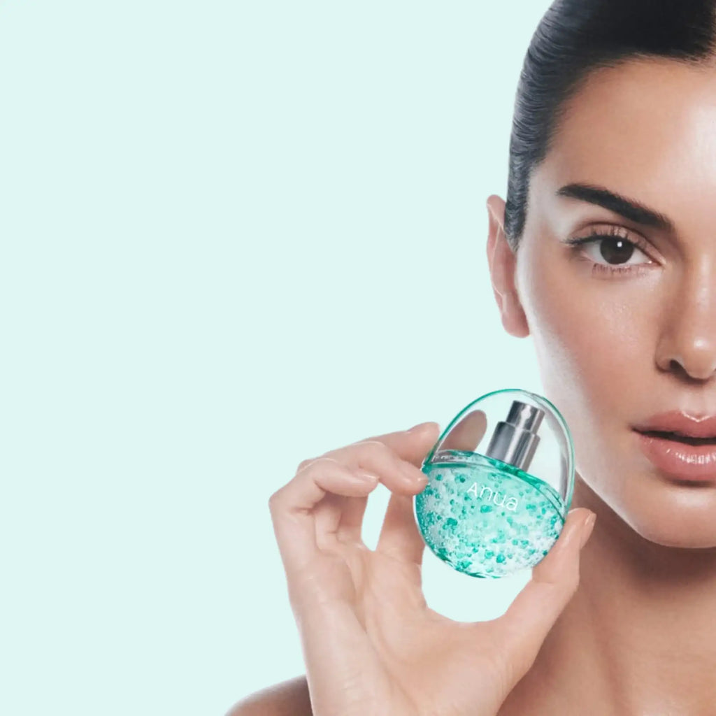 A translucent teal glass perfume bottle with a silver spray nozzle and the brand name ’anua’ printed on its side.