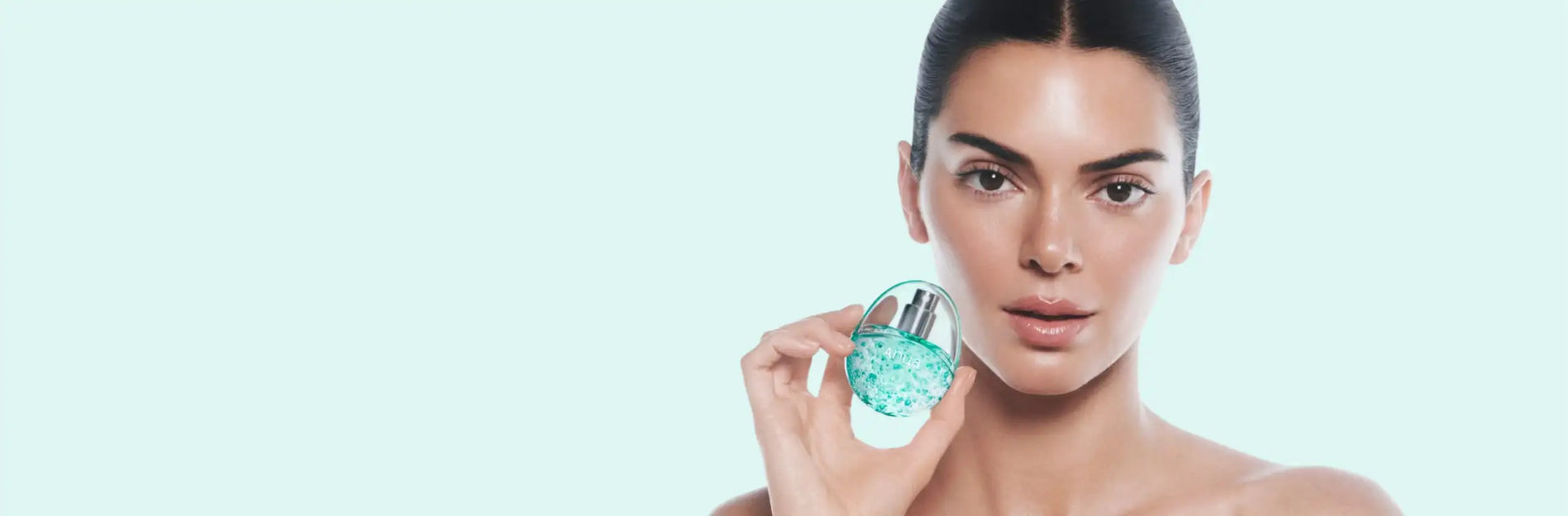A transparent, oval-shaped perfume bottle with a sleek silver cap and vibrant turquoise liquid inside.