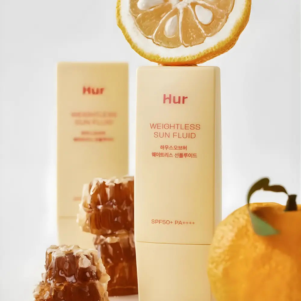 Creamy beige rectangular bottle of weightless sun fluid sunscreen with spf 50 pa++++ topped by a citrus slice