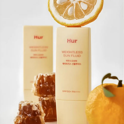 Creamy beige rectangular bottle of weightless sun fluid sunscreen with spf 50 pa++++ topped by a citrus slice